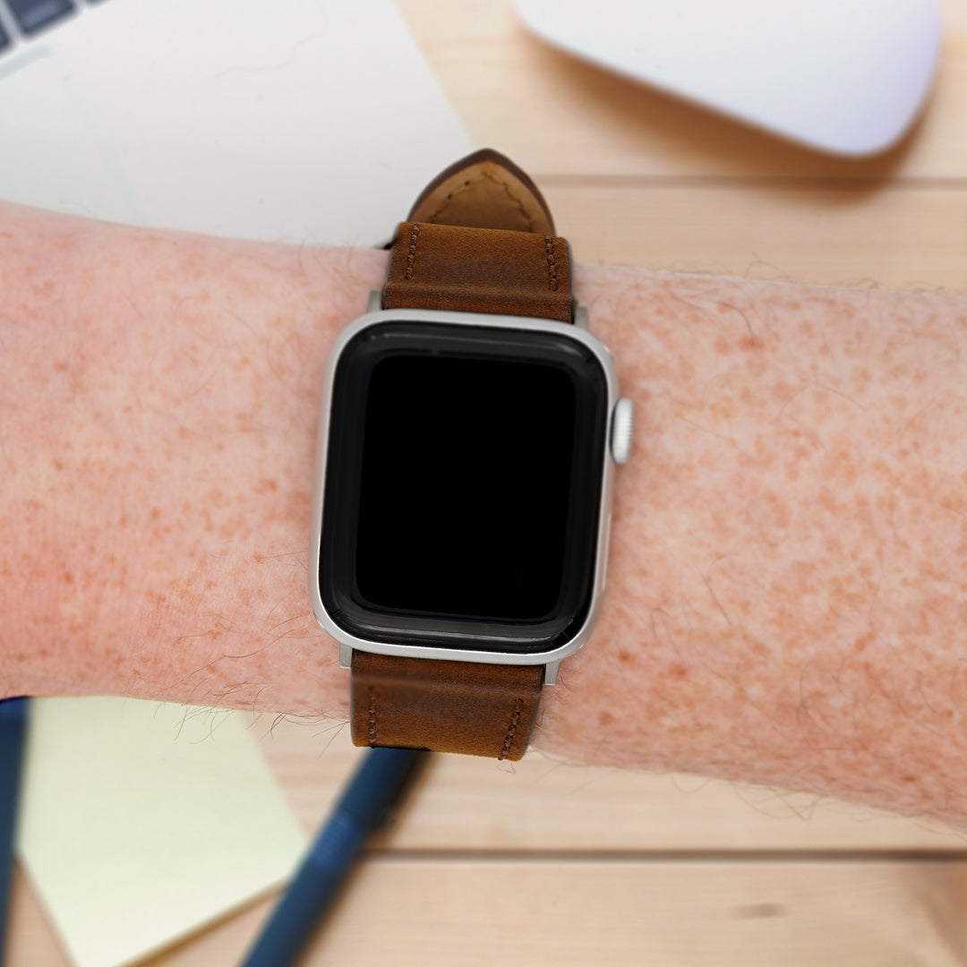 Smartwatch with a brown leather strap on a wrist, blurred background #color_dark-brown