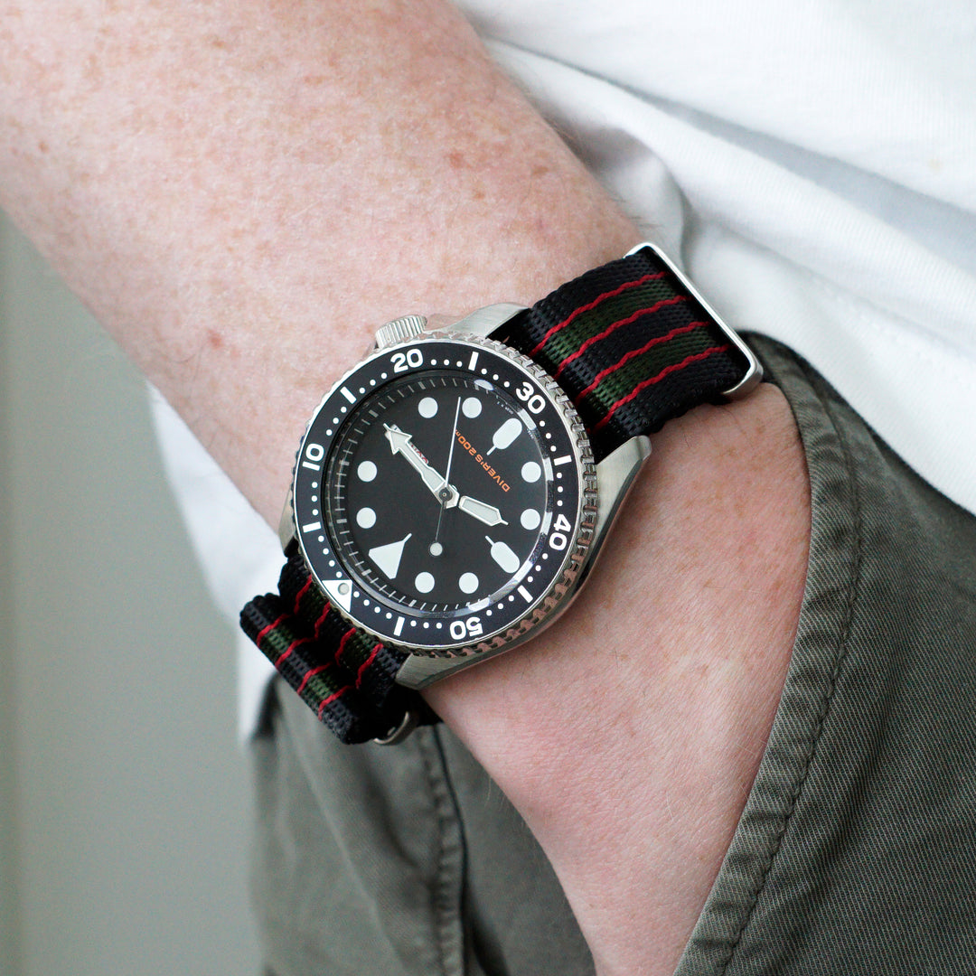 Wrist wearing a watch with a black face and red accents on a neutral background #color_black-red-and-green-regimental-striped