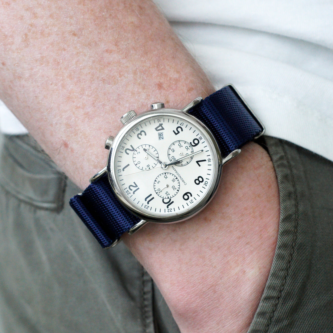 Wrist wearing a watch with a blue strap on a neutral background #color_navy-blue