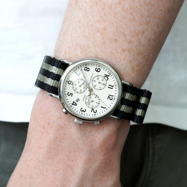 Wrist wearing a watch with a black and white striped strap on a neutral background #color_black-and-grey-regimental-striped