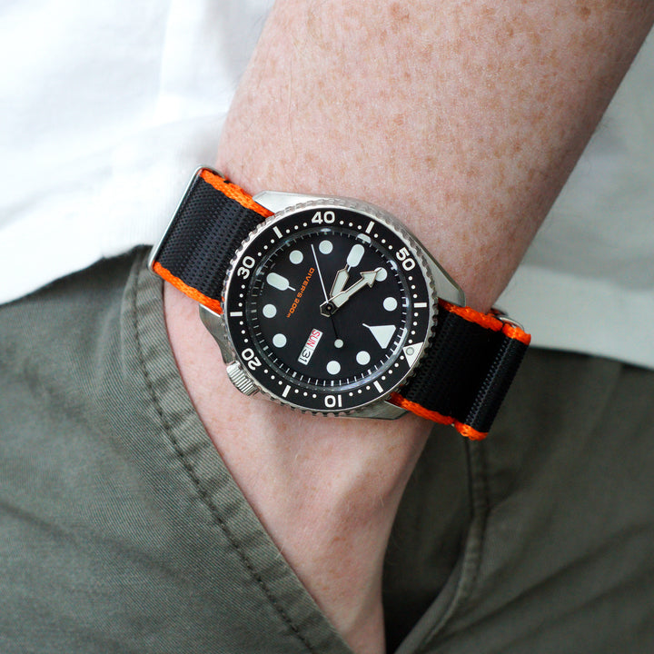Watch with black and orange strap on a wrist, wearing a green jacket. #color_black-with-orange-edge