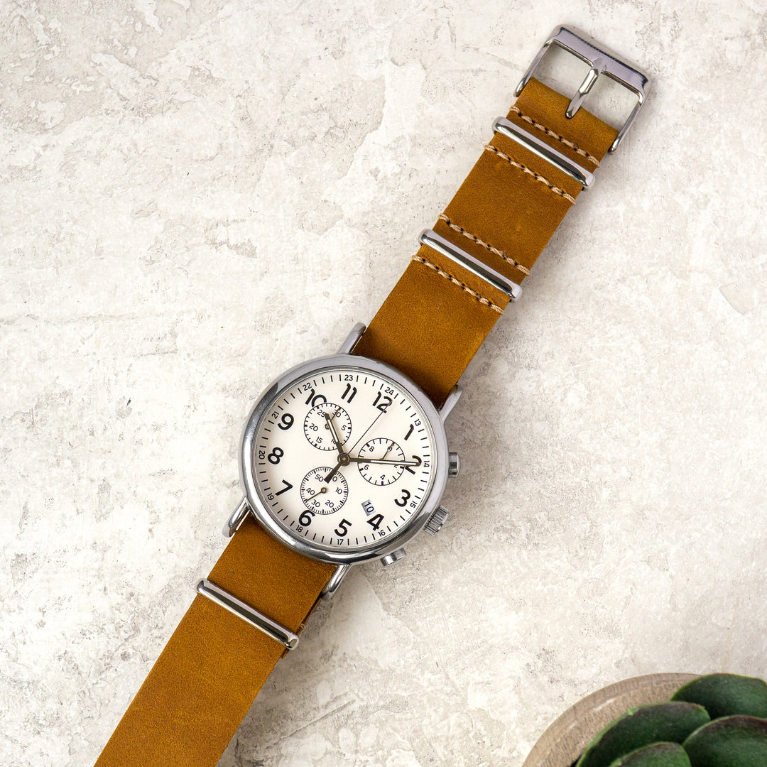 Wristwatch with brown leather strap and silver case on a textured surface #color_sand