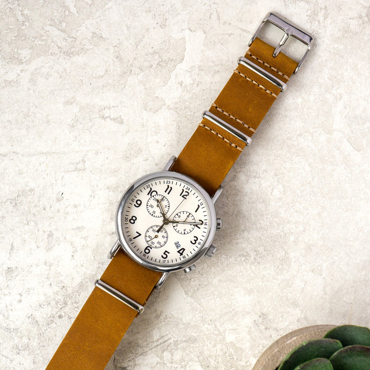 Wristwatch with brown leather strap and silver case on a textured surface #color_sand