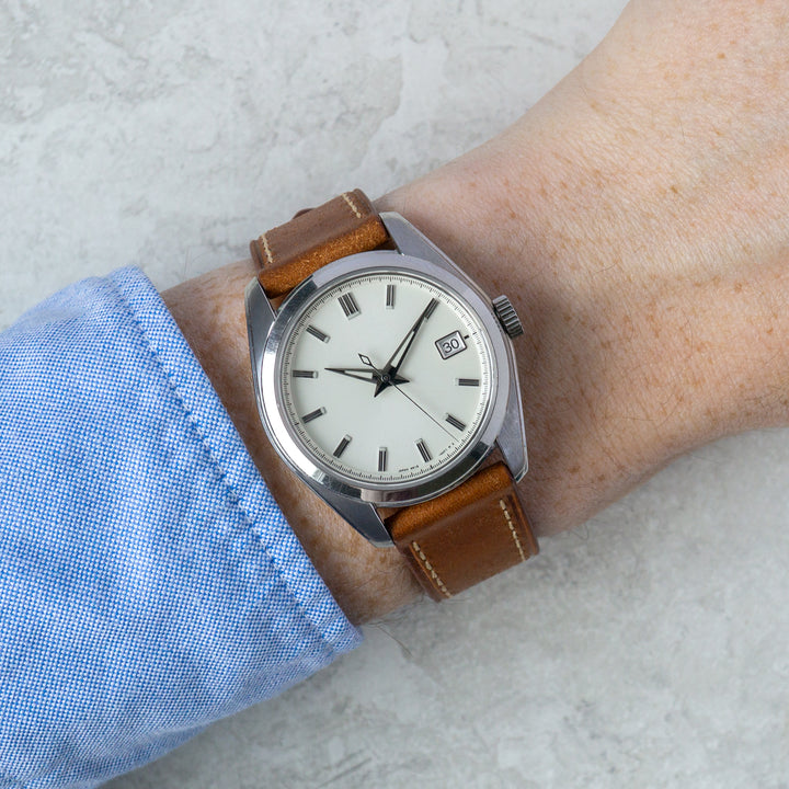 Wrist wearing a watch with a brown leather strap on a light background #color_cognac