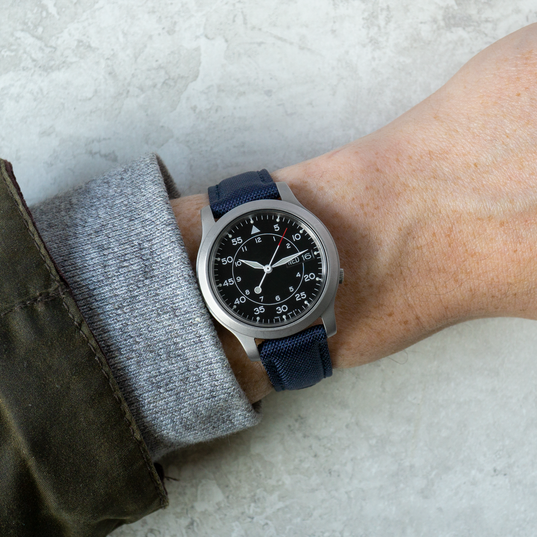 Wrist wearing a watch with a blue strap on a light gray background #color_navy-blue