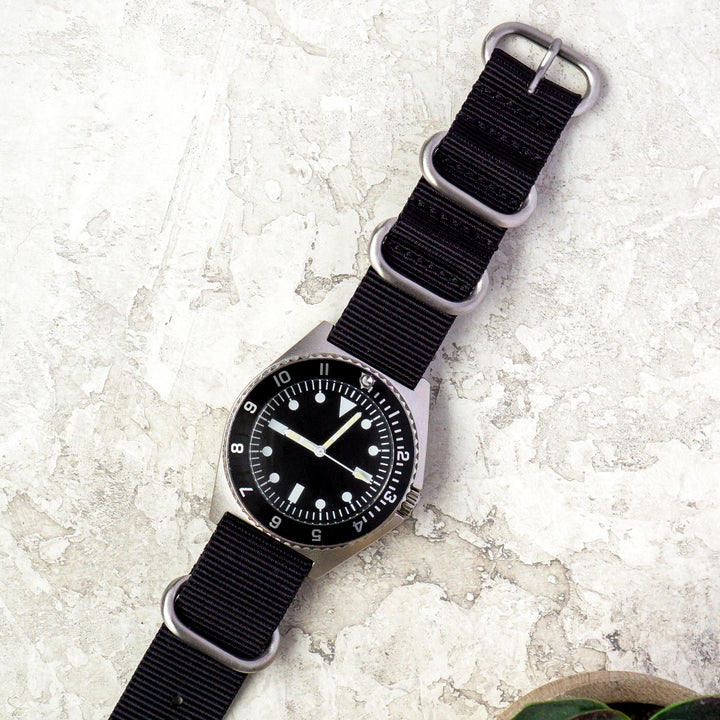 Black wristwatch with a black nylon strap on a light stone surface #color_black