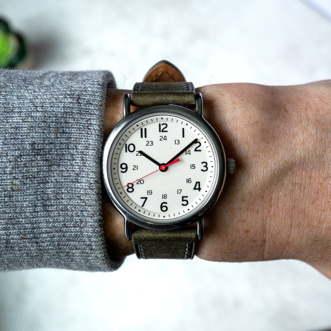 Wristwatch with grey leather strap on a wrist, wearing a gray sleeve. #color_grey