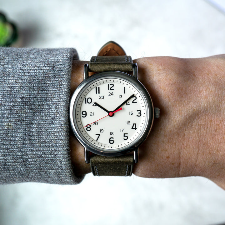 Wristwatch with grey leather strap on a wrist, wearing a gray sleeve. #color_grey