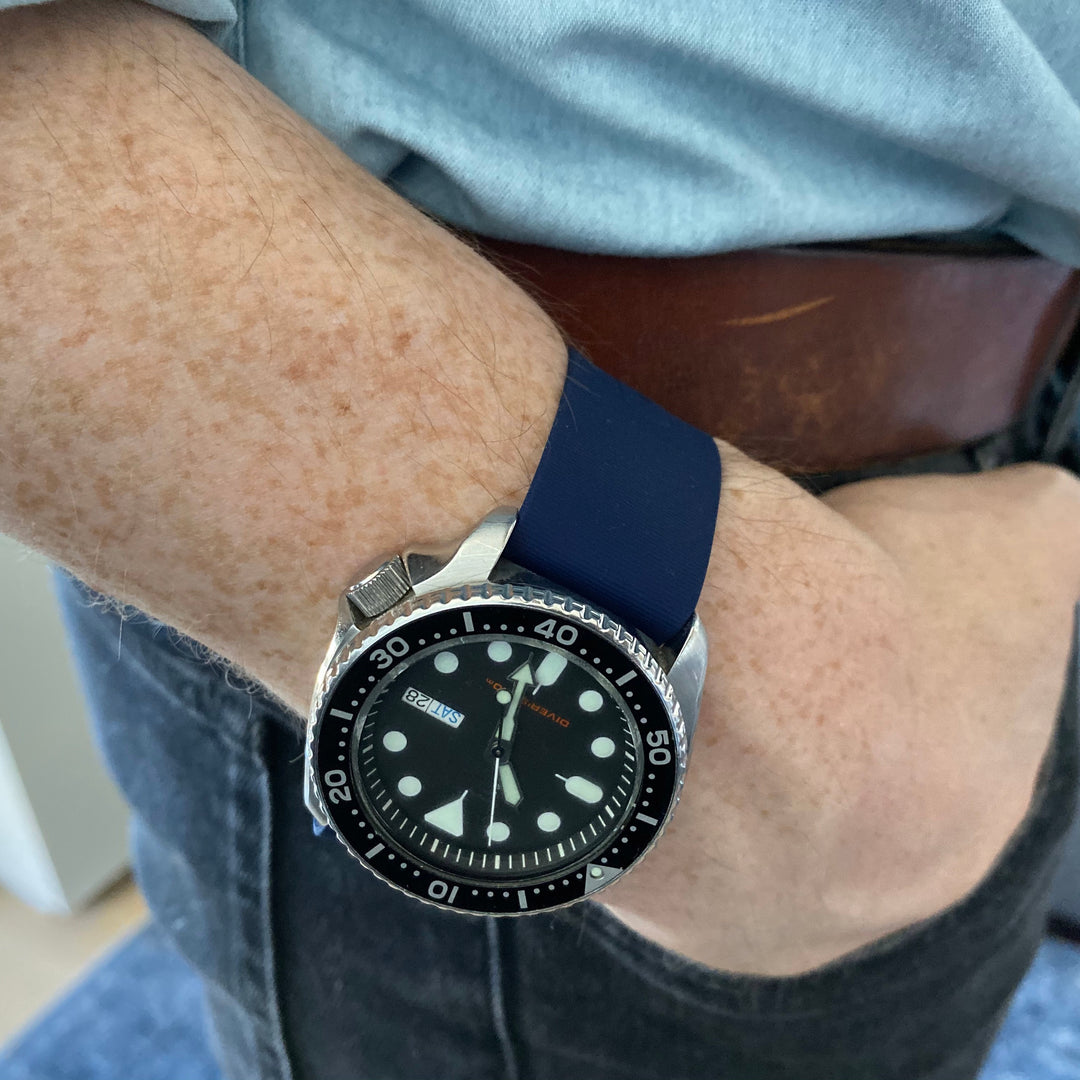 Person wearing a watch with a blue strap on their wrist. #color_navy-blue
