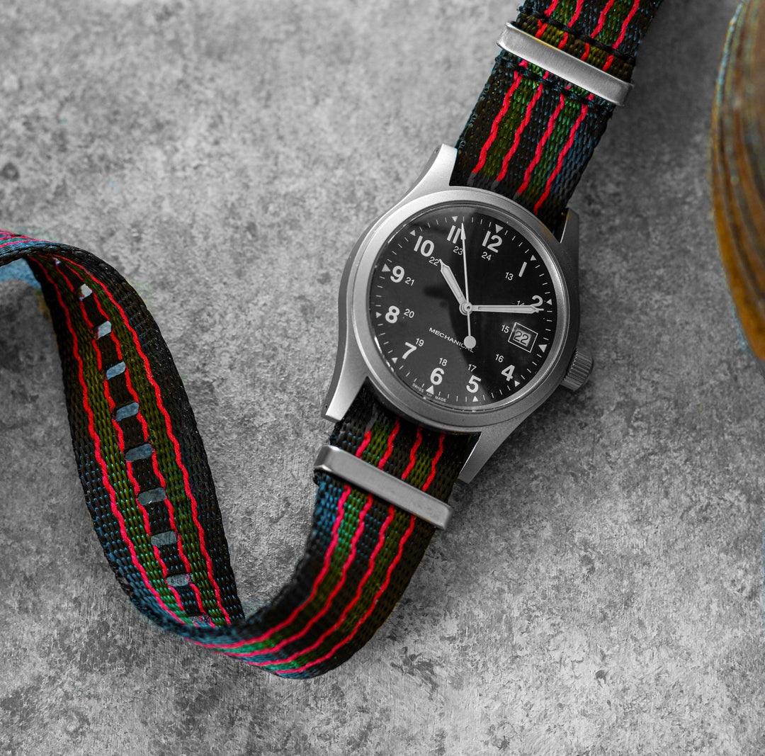 Watch with a black, red, and green striped strap on a gray surface #color_black-red-and-green-regimental-striped