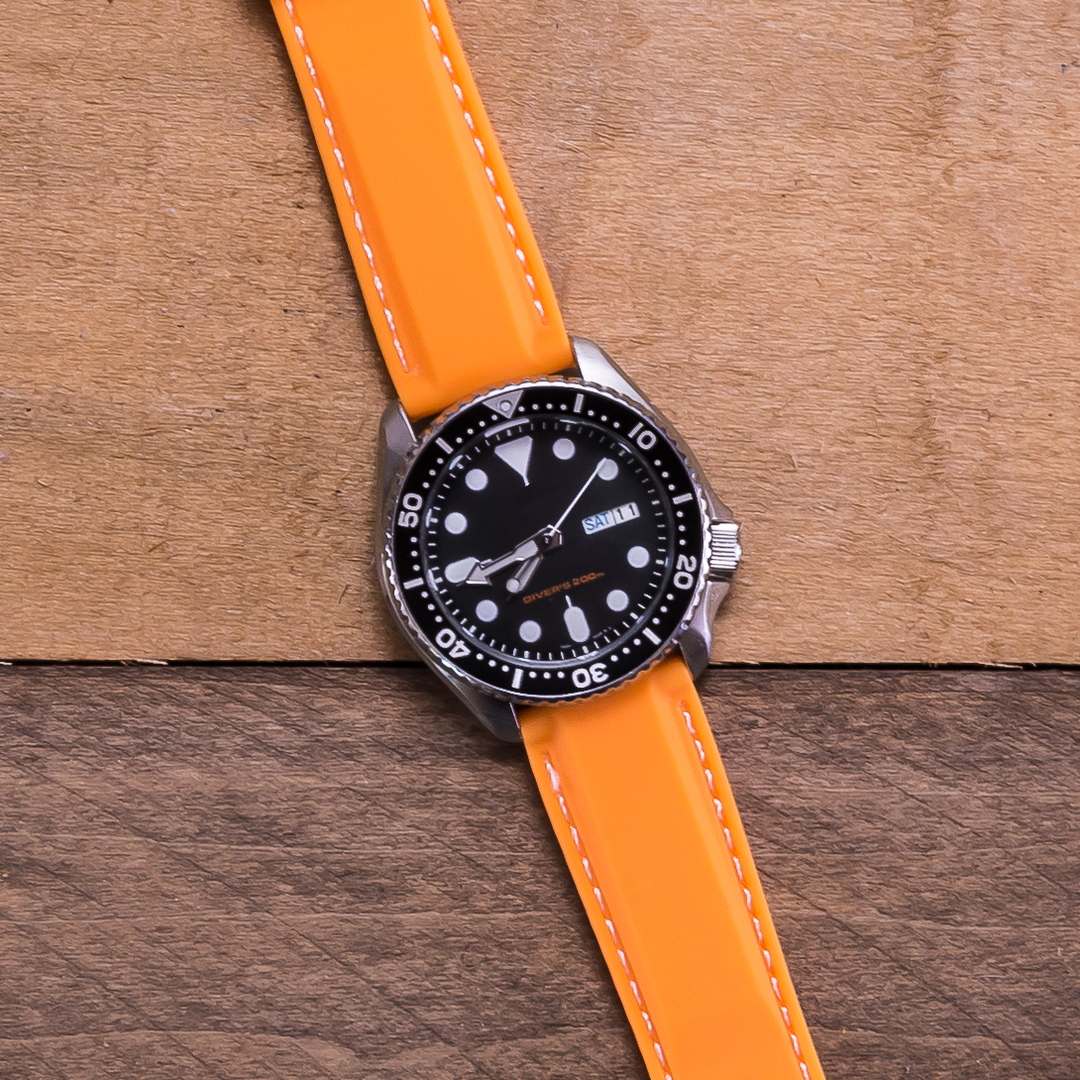 Watch with an orange strap on a wooden surface #color_orange-with-white-stitching