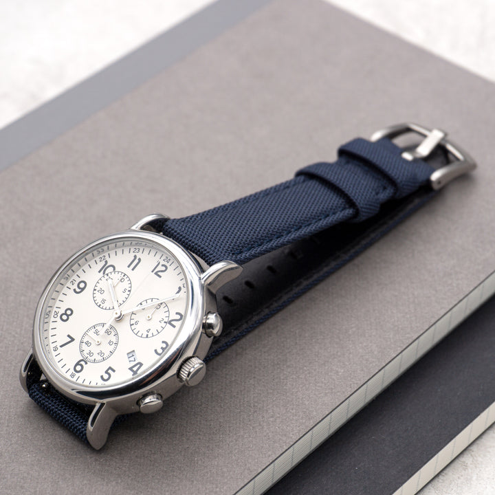 Wristwatch with blue strap and silver case on a gray surface #color_navy-blue