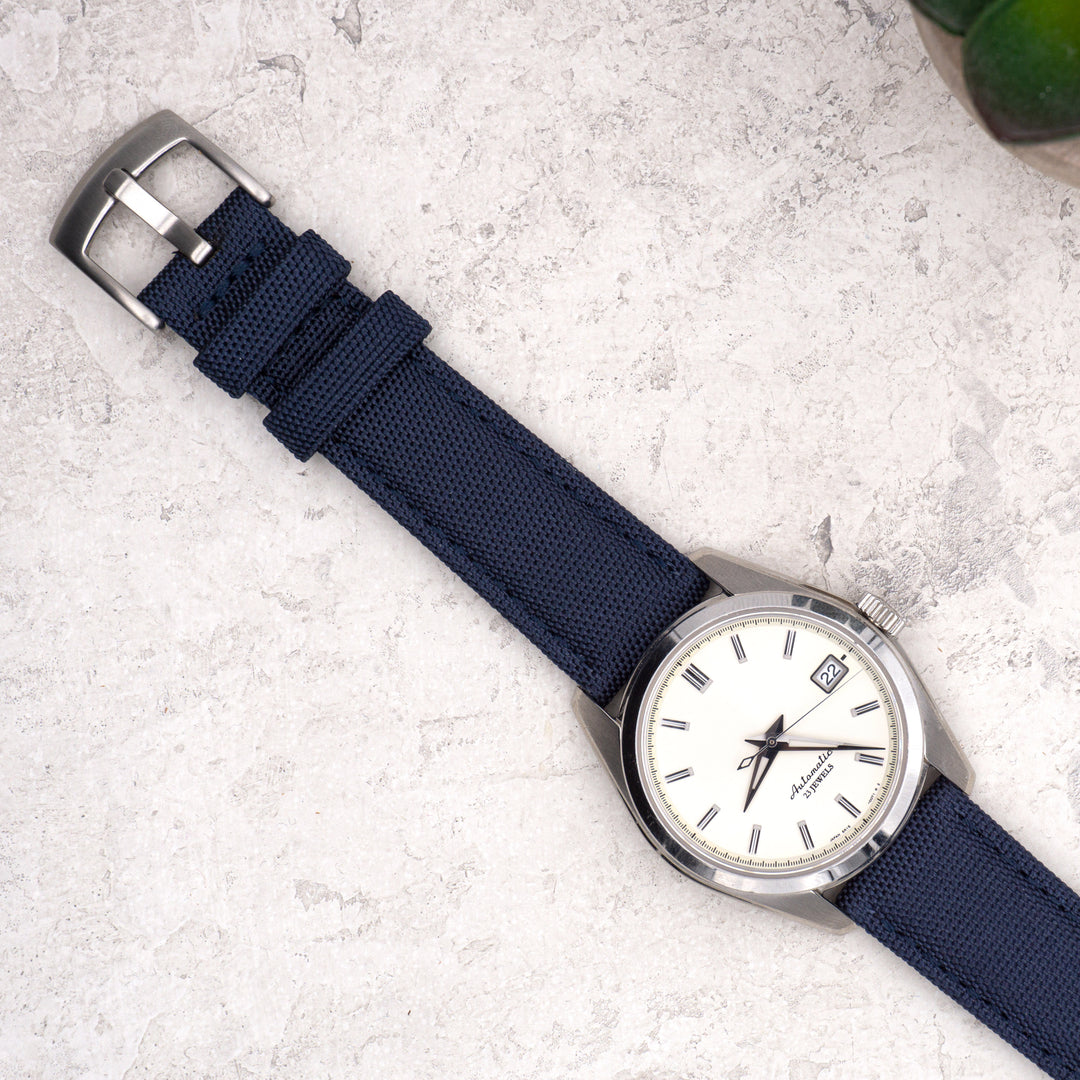Watch with a blue strap and silver case on a light gray surface #color_navy-blue