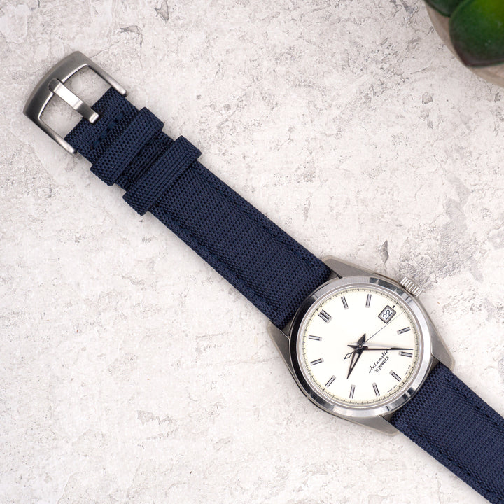 Watch with a blue strap and silver case on a light gray surface #color_navy-blue