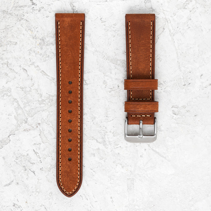 Brown leather watch strap with stitching on a light gray textured background #color_cognac