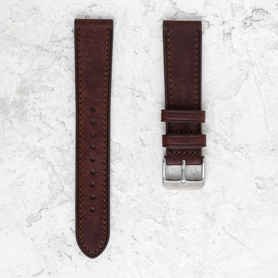 Brown leather watch strap with silver buckle on a textured white surface #color_dark-brown