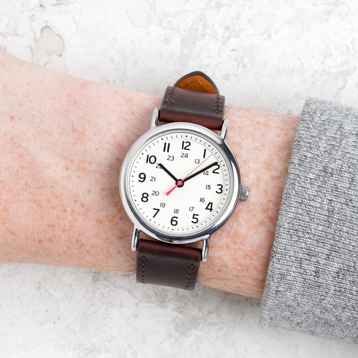 Wrist wearing a watch with a brown leather strap on a light background #color_dark-brown