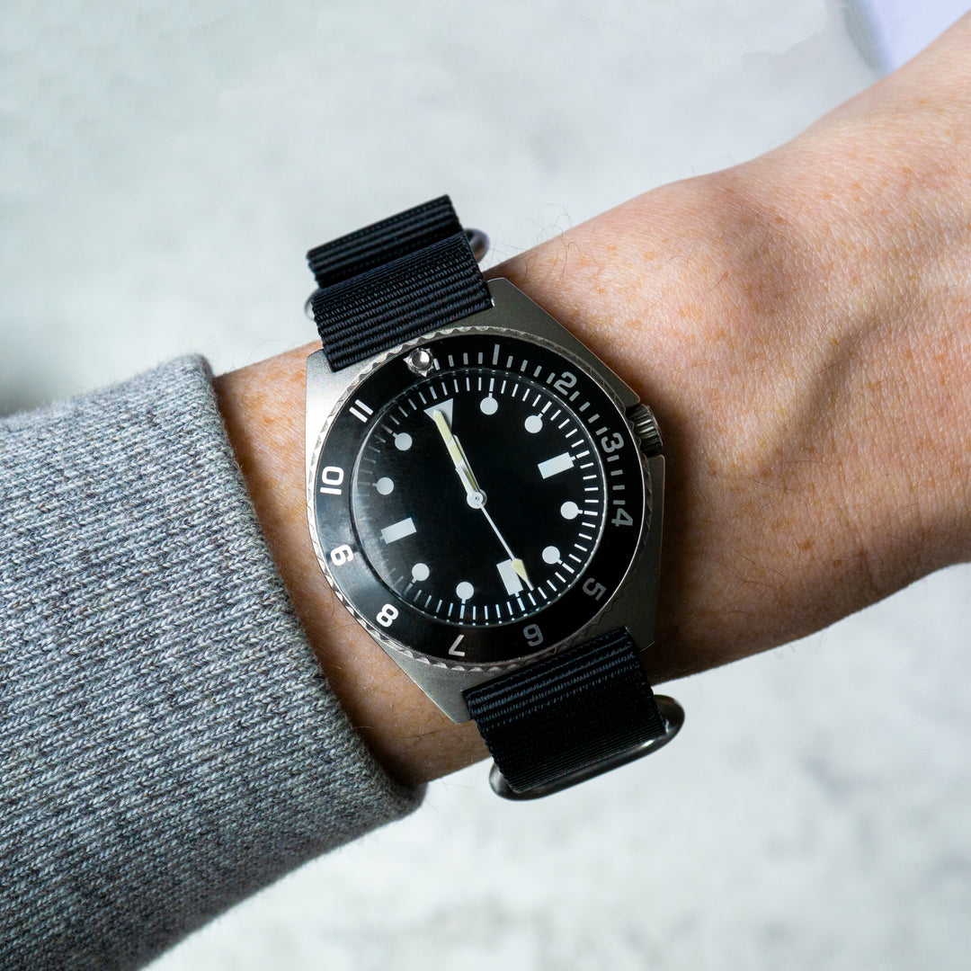 Black wristwatch with a black strap on a person's wrist against a light background #color_black