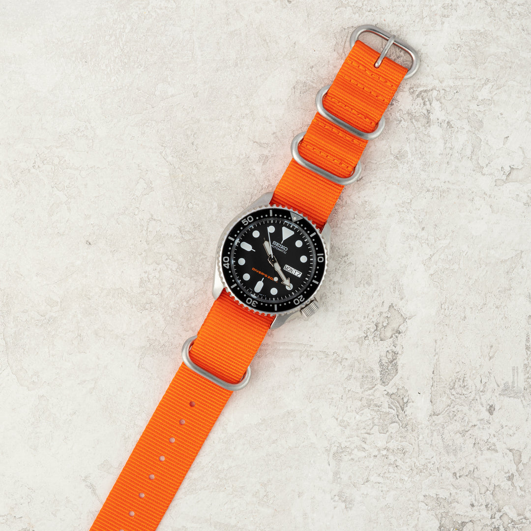 Watch with orange strap on a textured light gray surface #color_orange