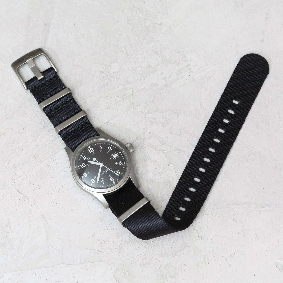 Wristwatch with black strap on a light gray textured surface #color_black