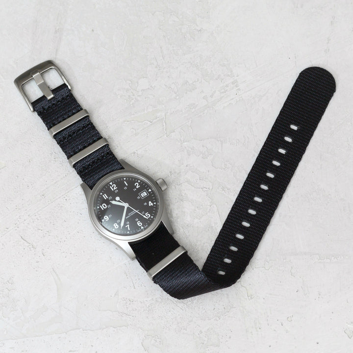 Wristwatch with black strap on a light gray textured surface #color_black