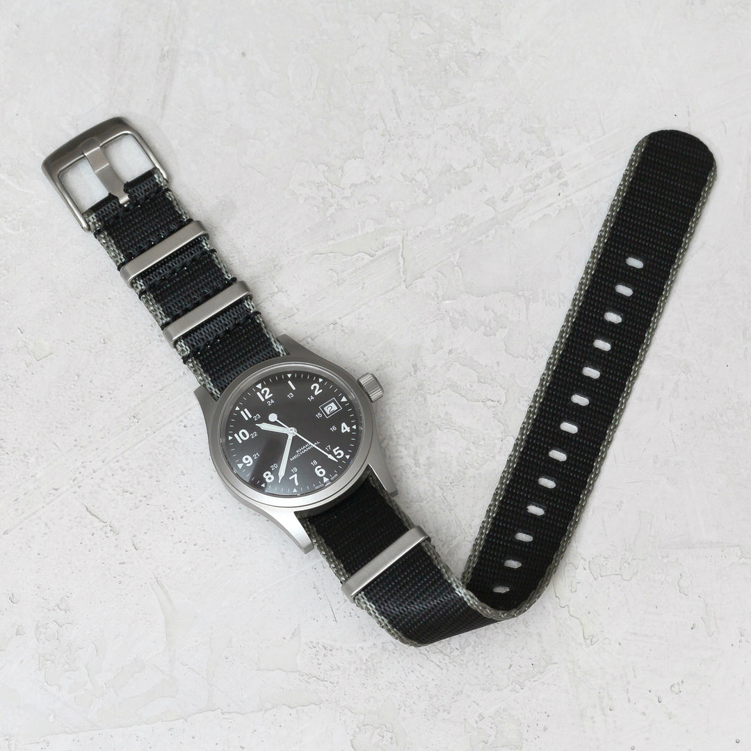 Watch with a black strap on a light gray textured surface #color_black-with-grey-edge